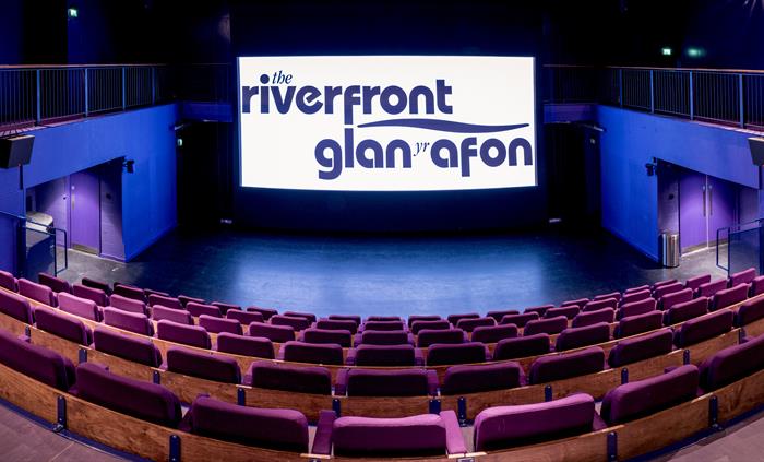 An empty cinema space with a projector with the theatre logo.